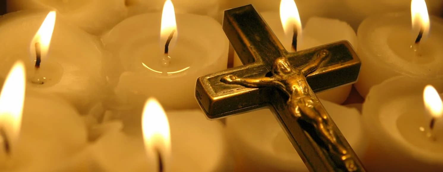 White candles with a gold crucific laying on top of them