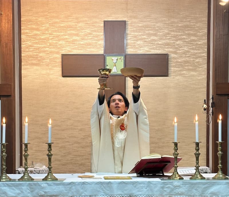 Head priest holding the wine cup and host above his head looking upwards